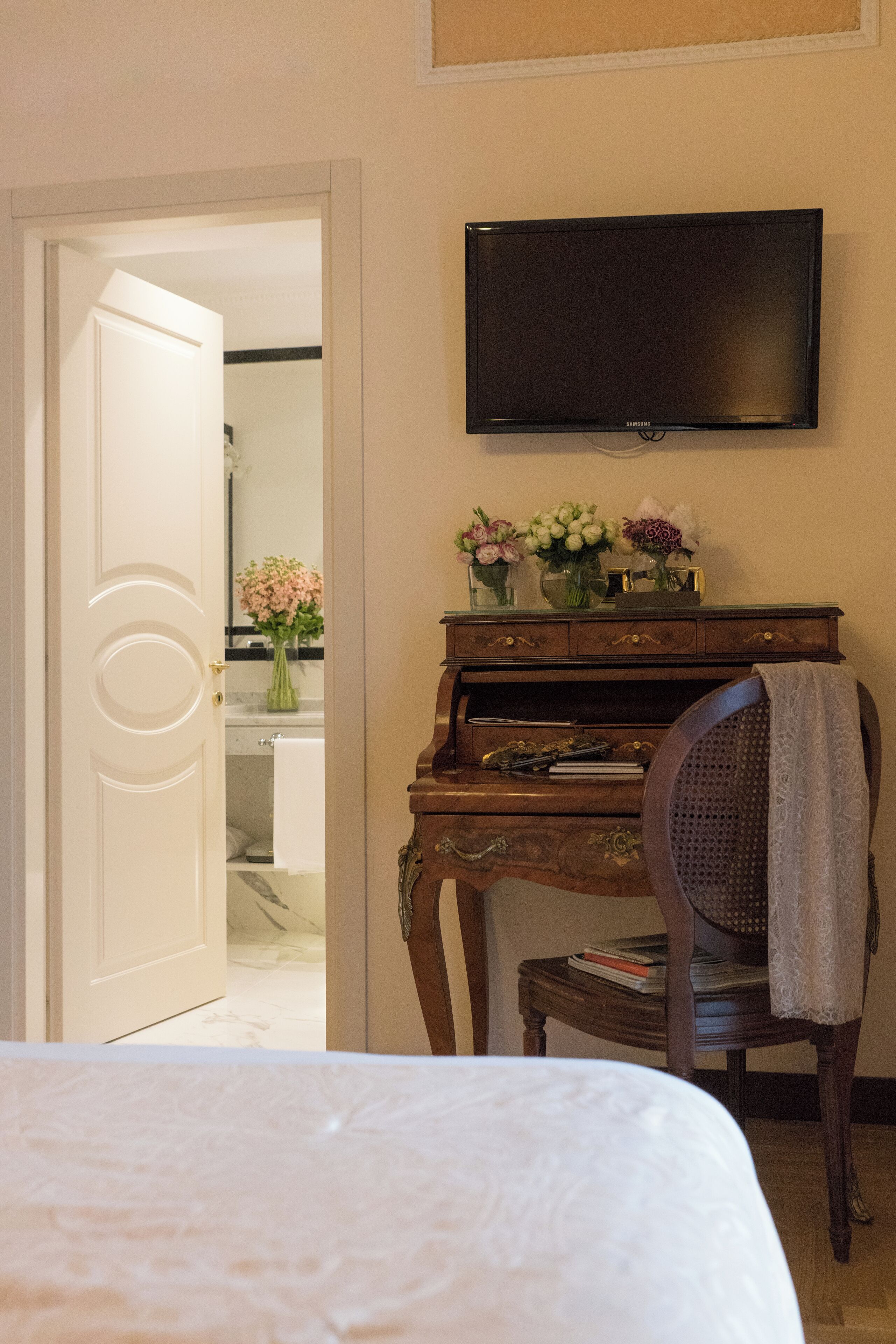 A hotel room with a bed, a wooden dresser, a television, and a bathroom visible through an open door.