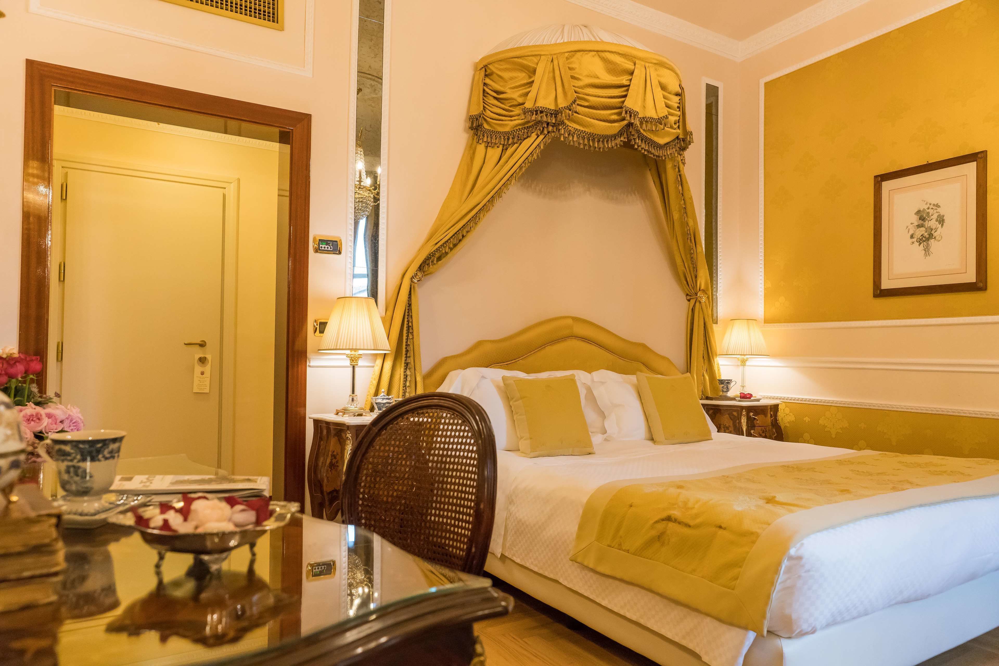 Habitación de hotel con cama, dos lámparas de noche, una mesa con frutero y un cuadro en la pared.