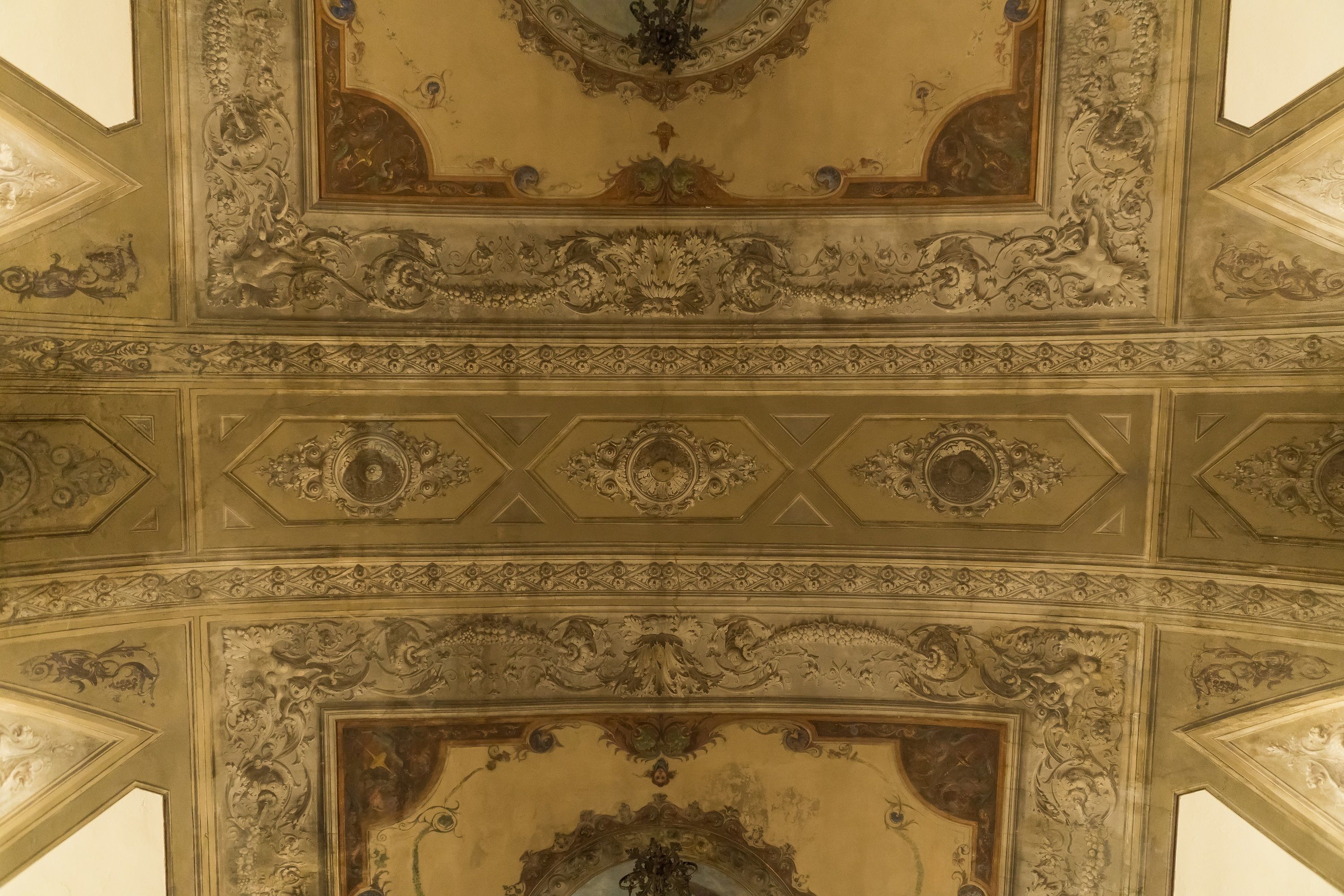 A detailed ceiling with ornate carvings and a central chandelier.