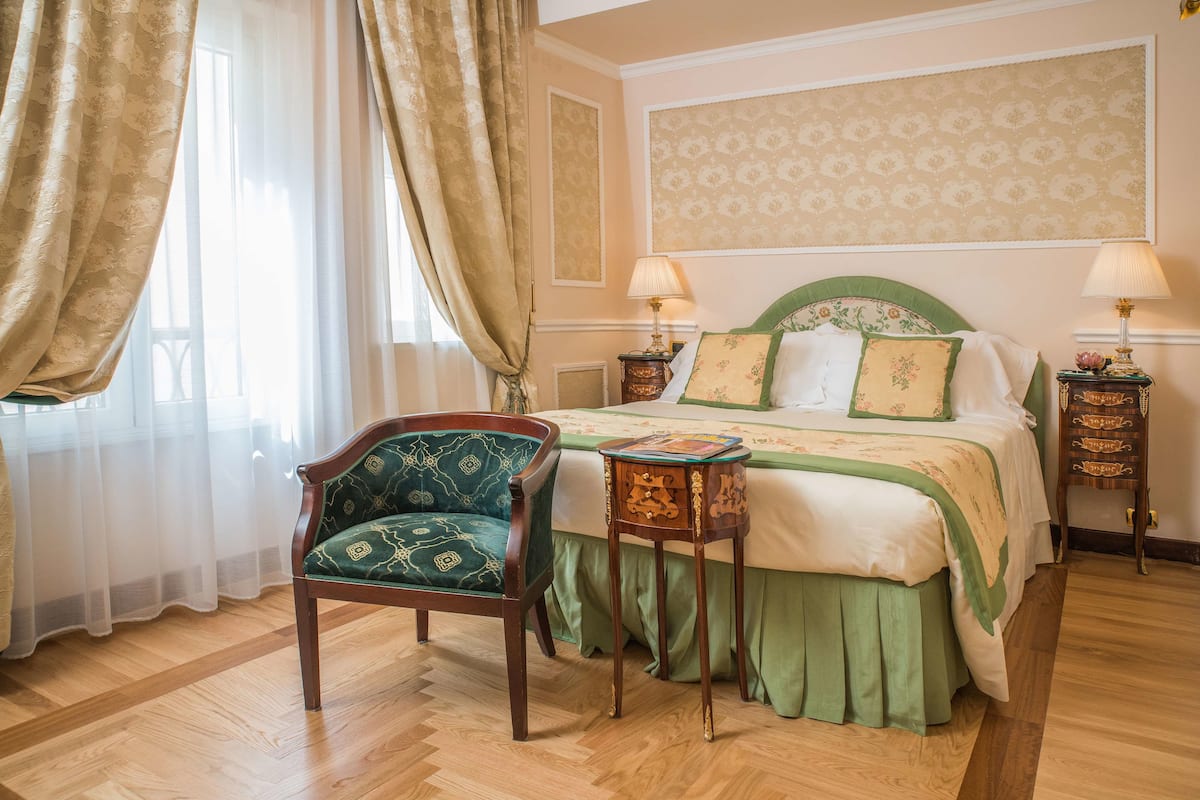 Ein Schlafzimmer mit einem Bett, einem Sessel, zwei Nachttischen und einem Fenster mit Vorhängen.