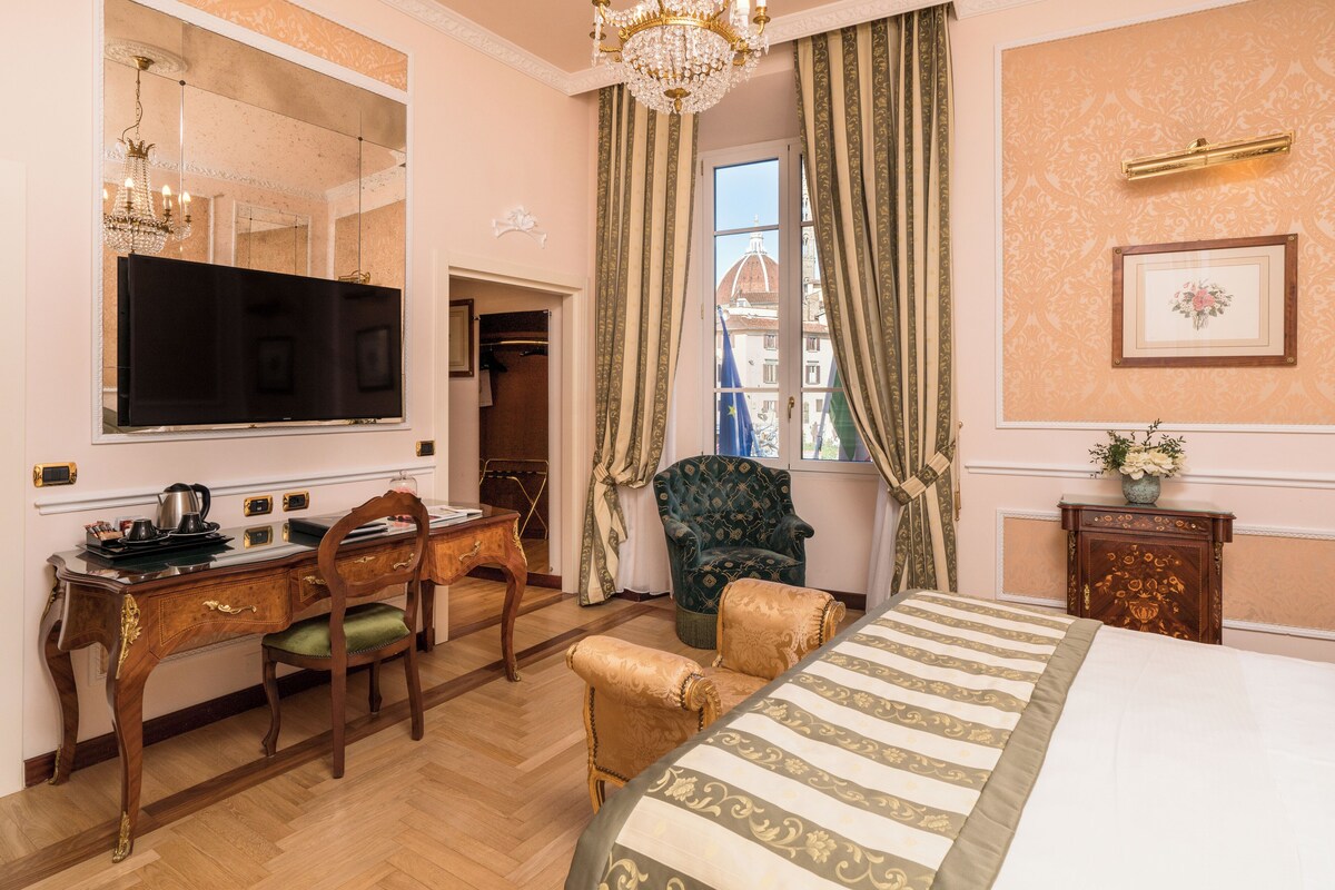 Une chambre d’hôtel avec un grand lit, un bureau avec un ordinateur, une chaise et une fenêtre avec des rideaux.