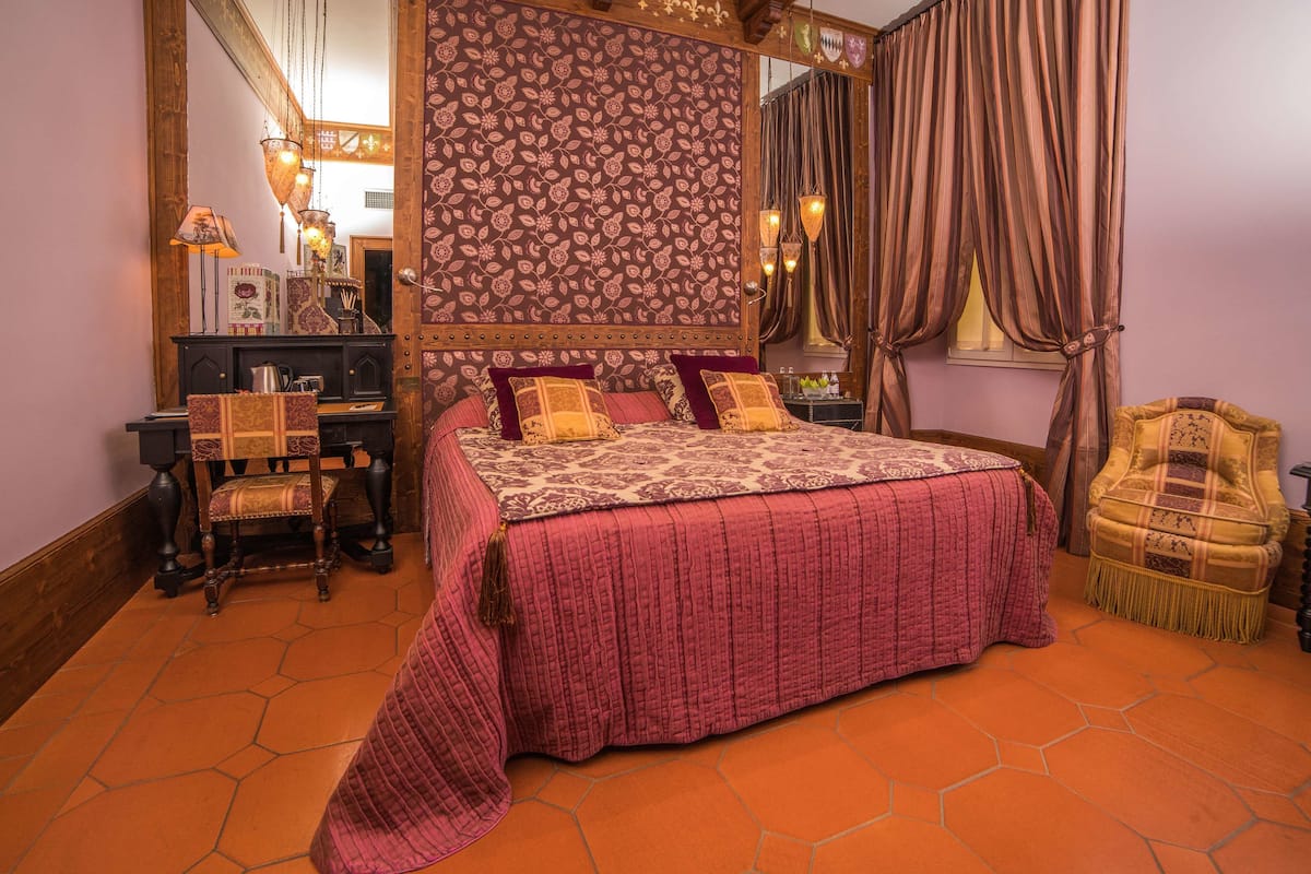 Ein Schlafzimmer mit einem großen Bett, einem Schreibtisch mit Stuhl, einem Spiegel und einem Fenster mit Vorhängen.