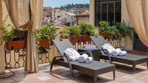 A balcony with two wicker lounge chairs, each with rolled towels, and potted plants.