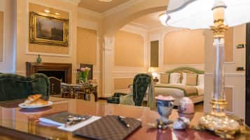 A hotel room with a bed, a desk with a lamp, a chair, a fireplace, and a painting on the wall.