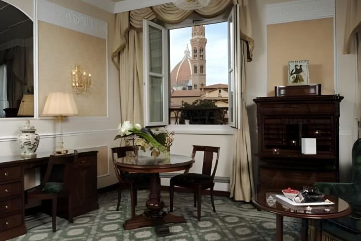 A room with a desk, chair, round table, and a view of a tower through a window.