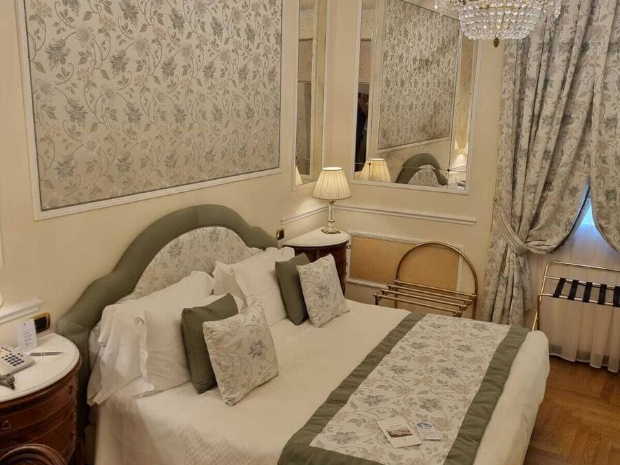 Un dormitorio ordenado con una cama grande, una mesita de noche, un espejo y una araña.