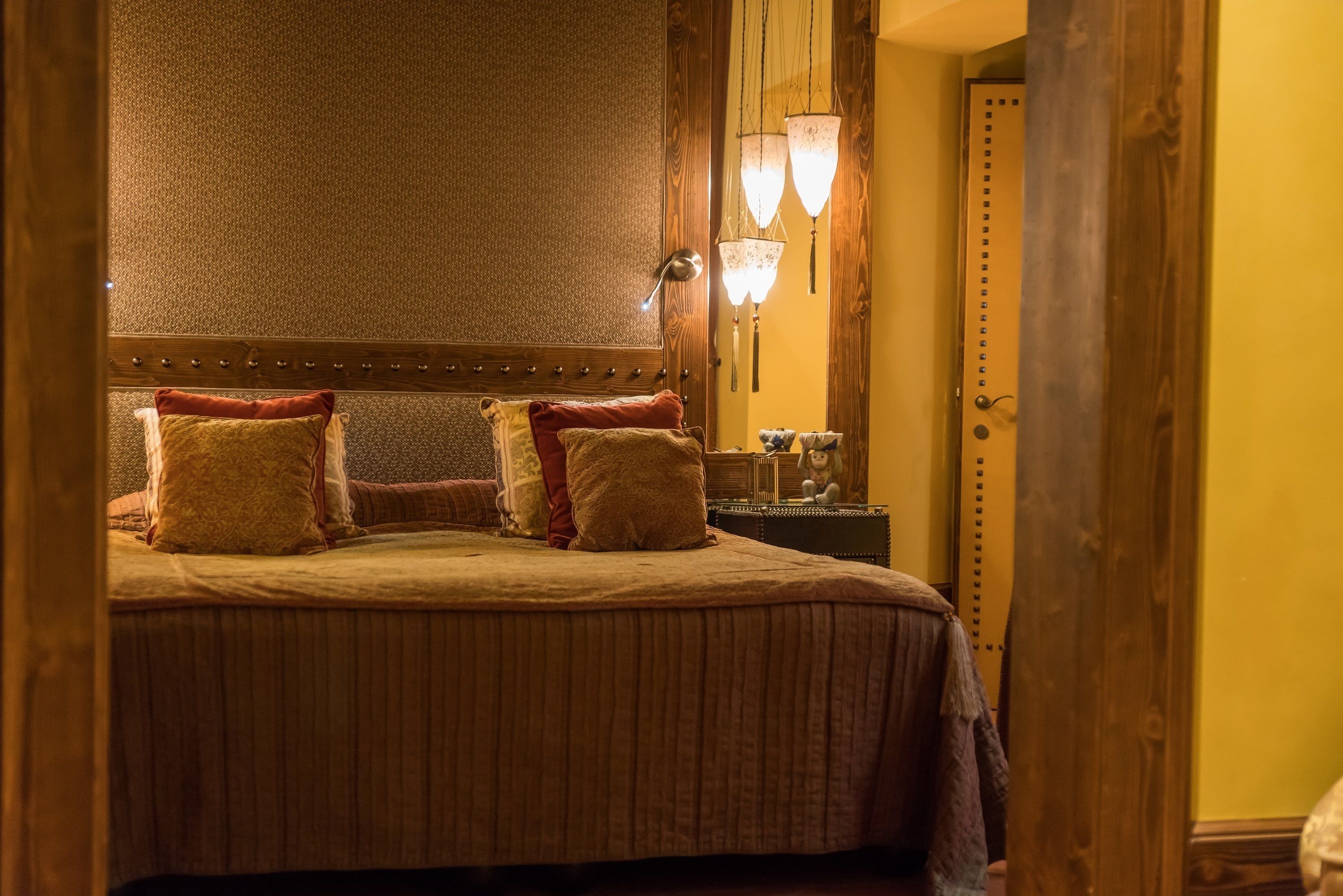 A neatly made bed with a wooden headboard, two bedside lamps, and a nightstand with a mirror and a small table.