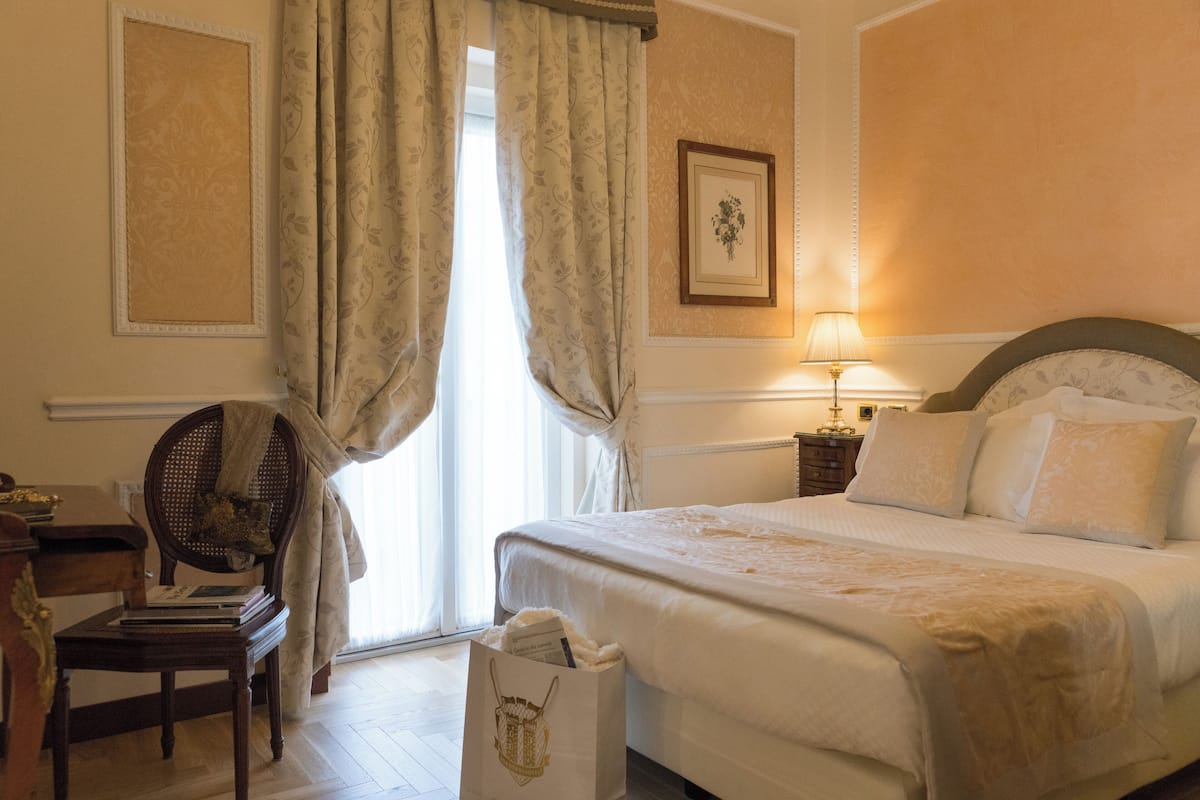 Ein Hotelzimmer mit einem großen Bett, einem Nachttisch mit Lampe, einem Sessel und einem Fenster mit Vorhängen.