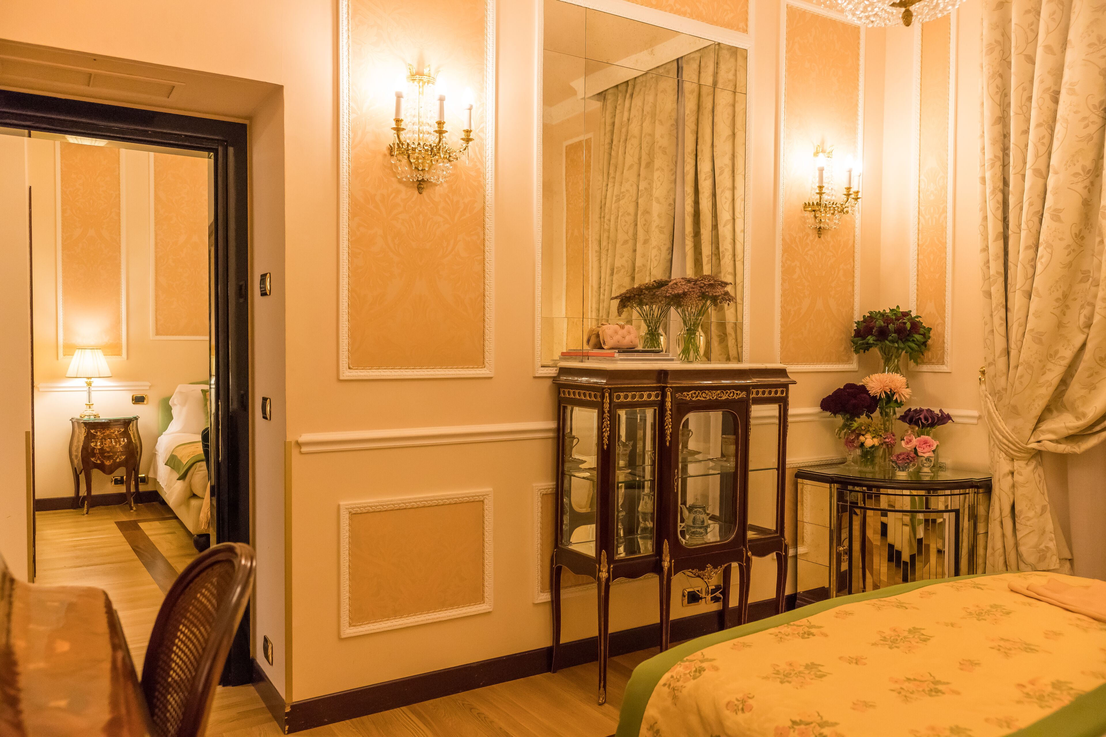 Une chambre d’hôtel avec un lit, un bureau, une chaise, un miroir et une petite table sur laquelle est posé un vase de fleurs.