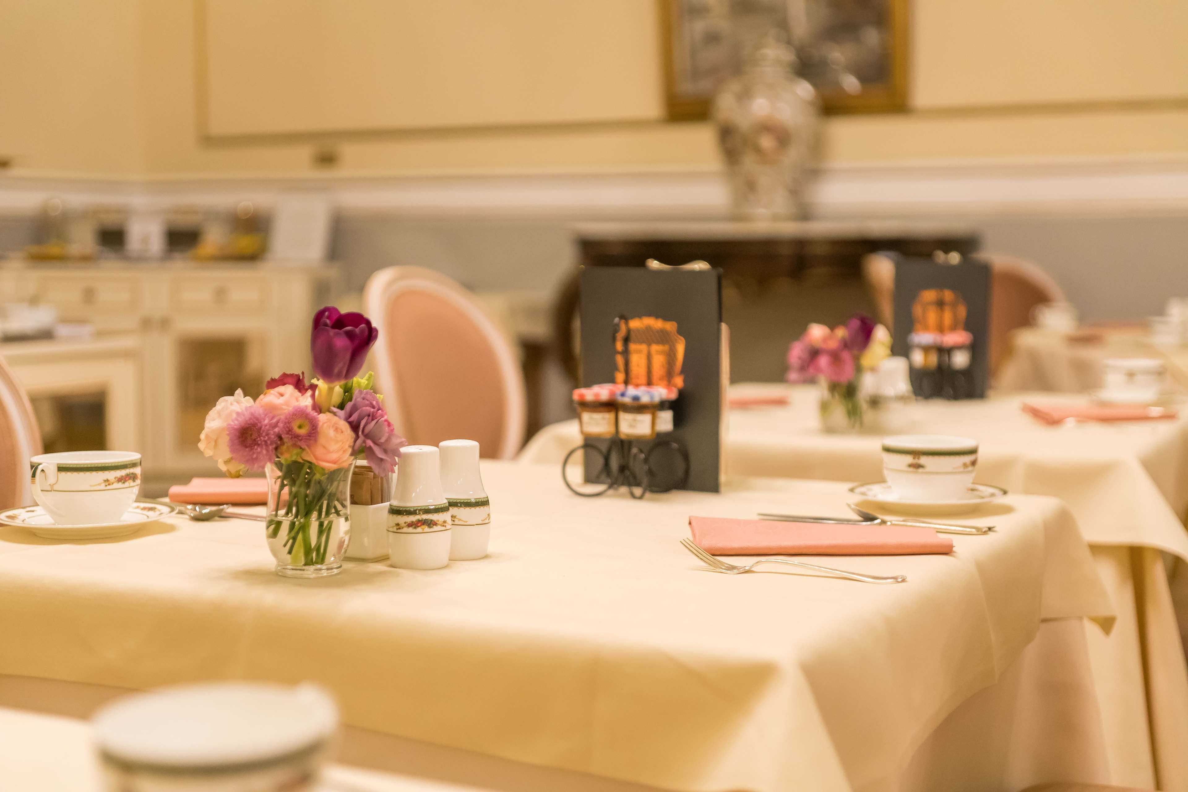 A dining area with tables set for service, including tea cups, vases with flowers, and a menu stand.