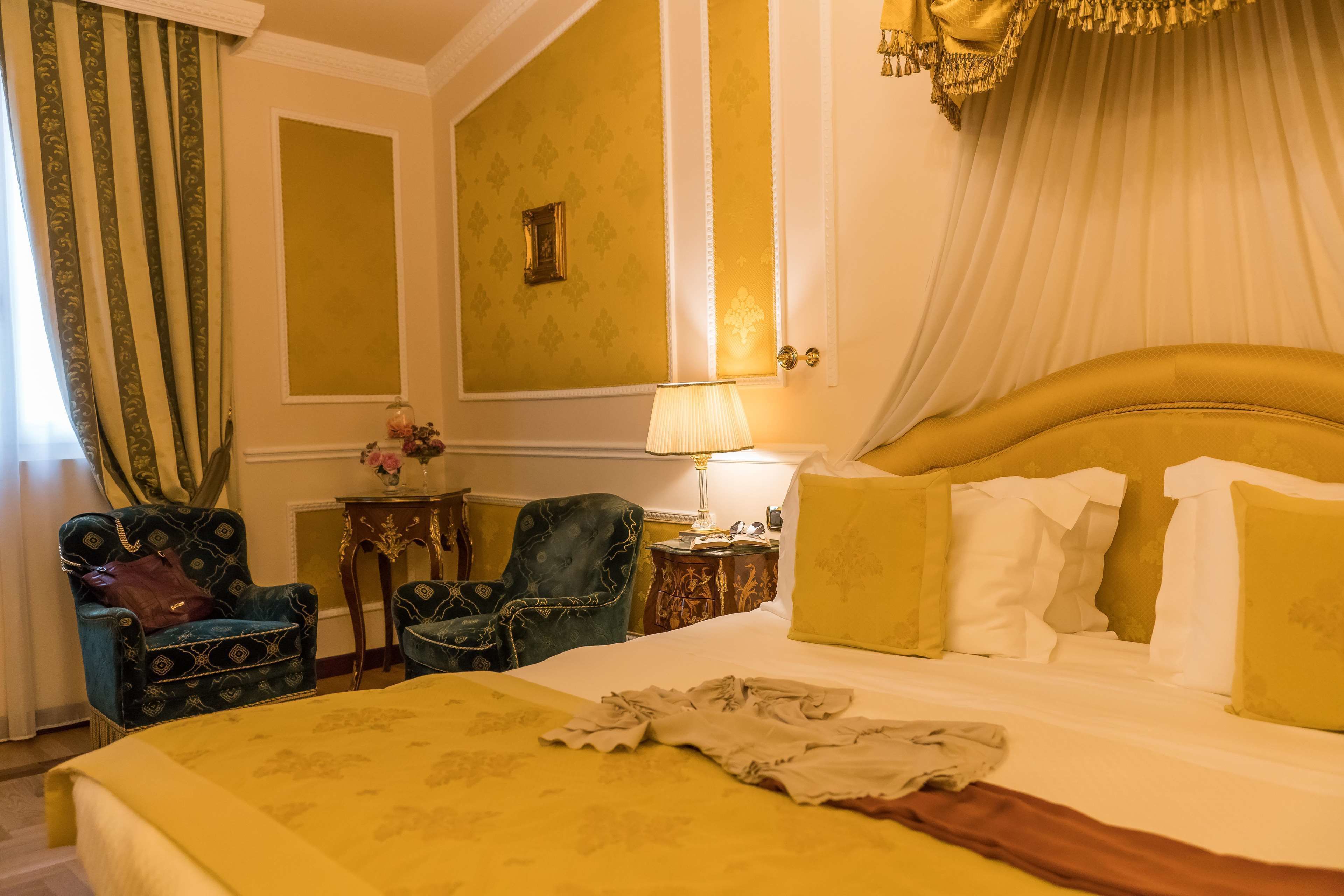 A hotel room with a large bed, two armchairs, a nightstand, and a lamp.