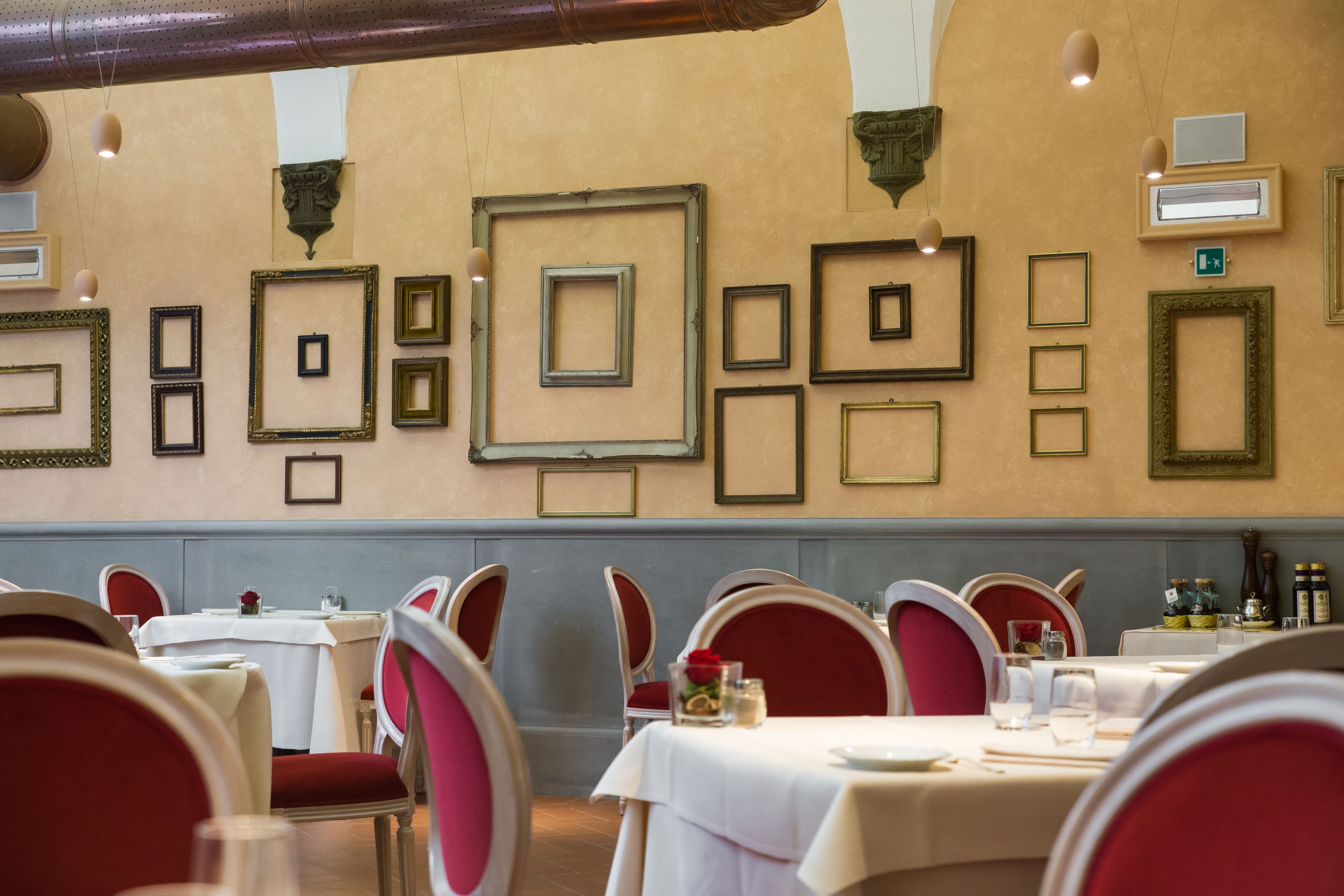 A dining area with tables set for service, red upholstered chairs, and framed pictures on the wall.