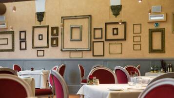 A dining area with tables set for service, red upholstered chairs, and framed pictures on the wall.