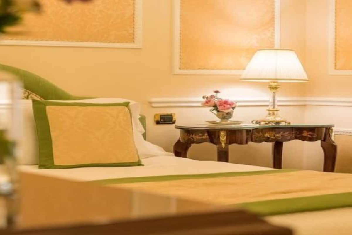 A hotel room with a bed, a nightstand, a lamp, and a vase with flowers.