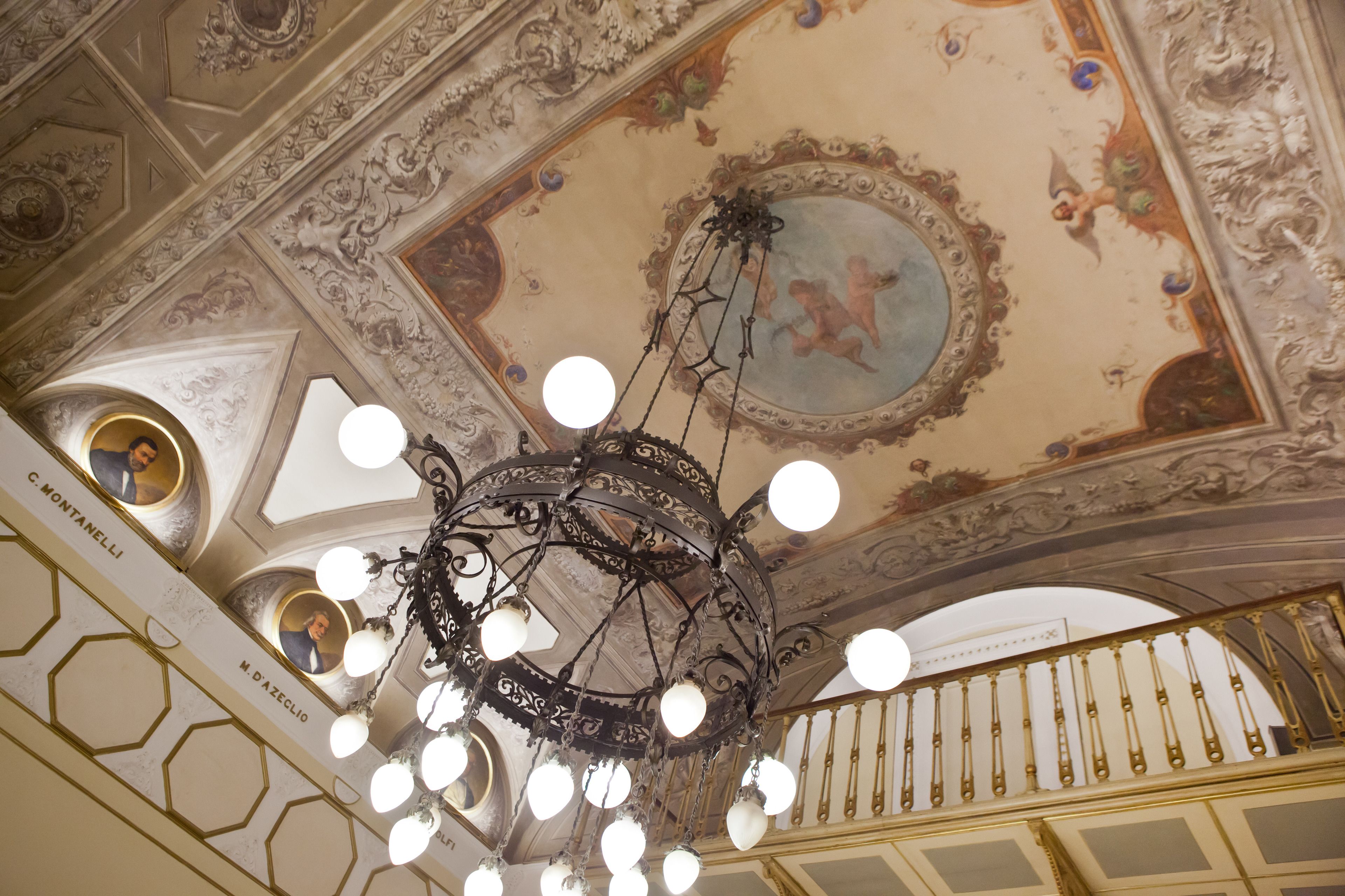 Un candelabro con múltiples luces esféricas colgando de un techo decorativo con diseños intrincados y un fresco.