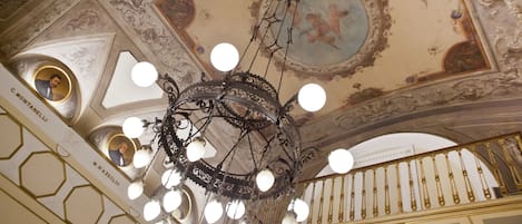 A chandelier with multiple spherical lights hanging from a decorative ceiling with intricate designs and a fresco.