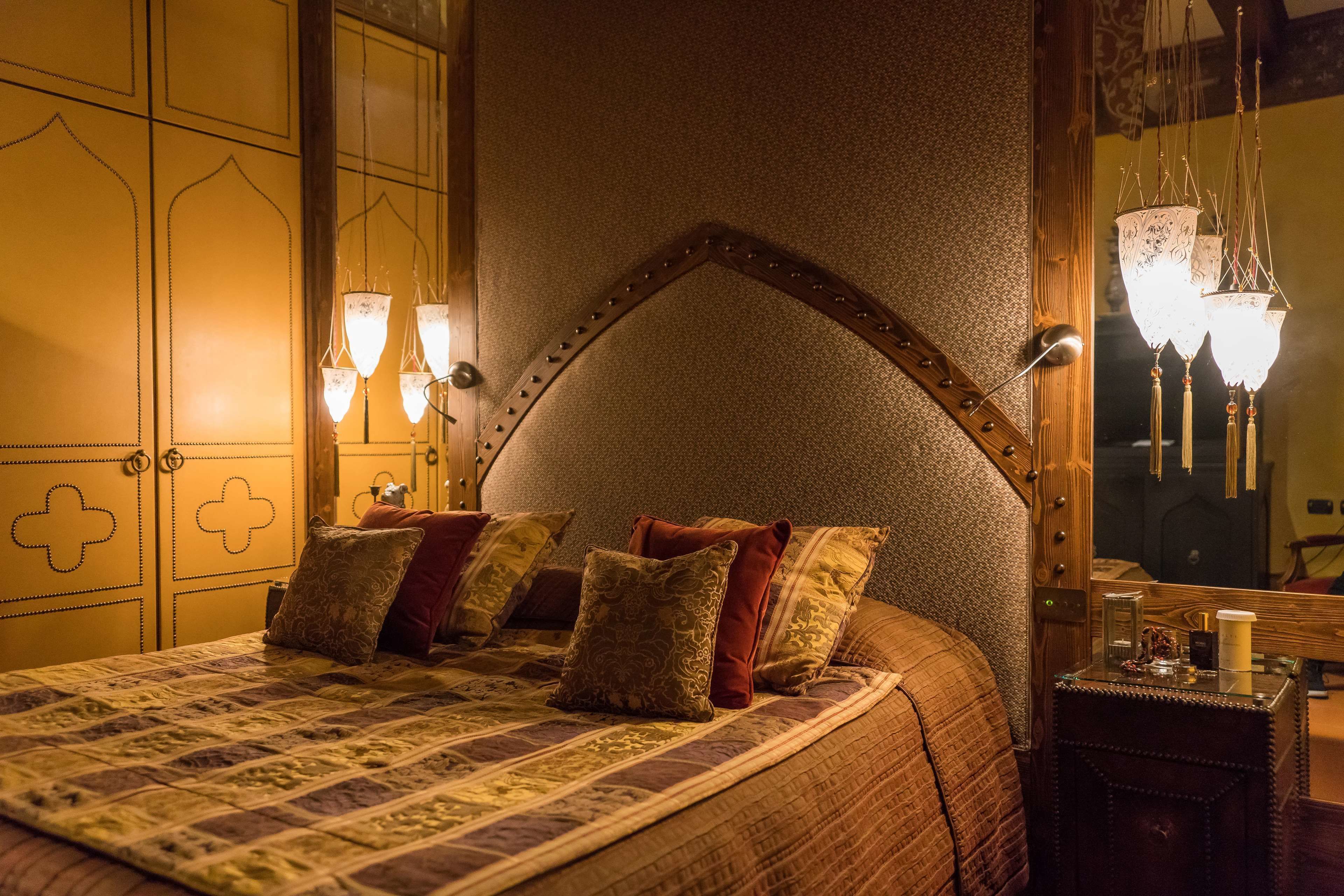 Ein Schlafzimmer mit einem großen Bett, mehreren Kissen, einem Holzkopfende, Wandleuchten und einem Nachttisch mit Lampe.