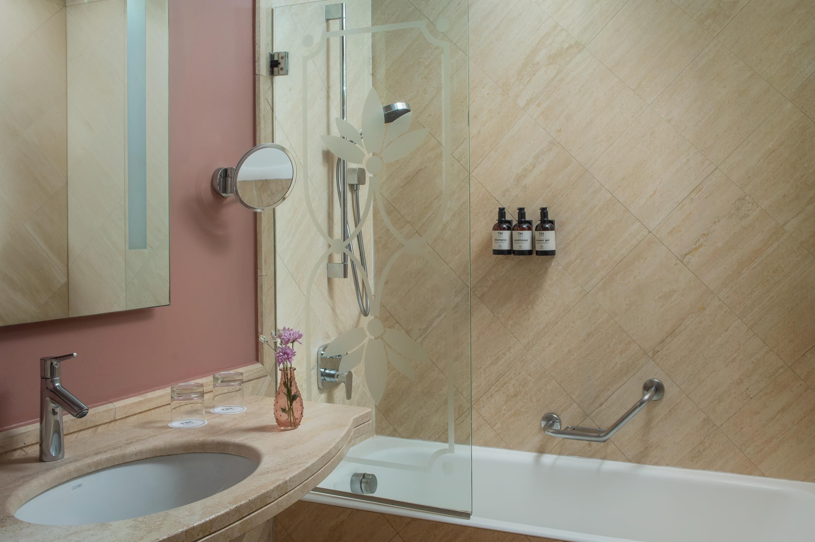 A bathroom with a sink, mirror, shower, and a glass-enclosed shower area.