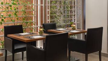 Un coin repas avec une table dressée pour deux personnes, entourée de chaises, et offrant une vue sur un mur de briques et une fenêtre ornée de plantes.