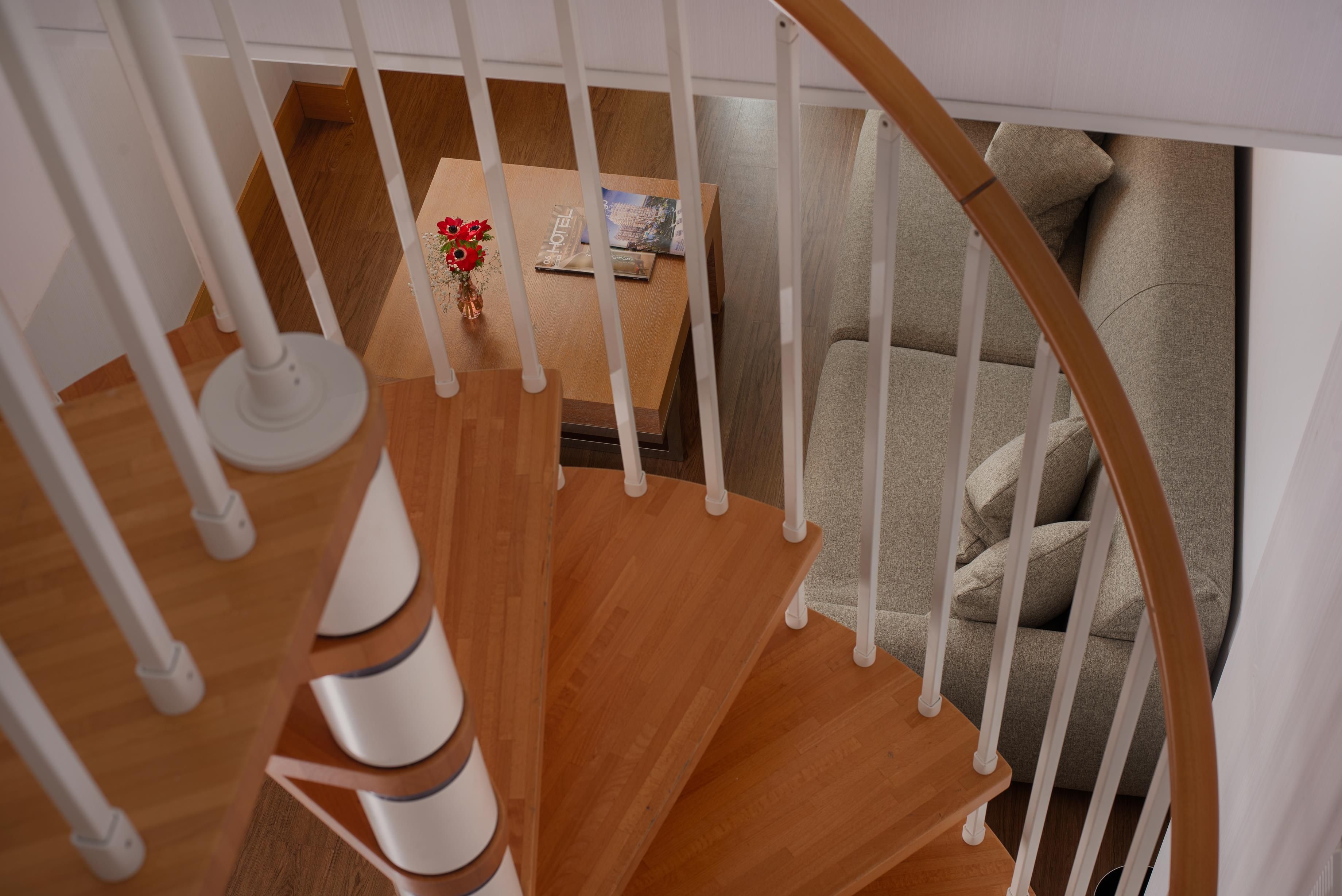 A wooden staircase with white balusters leading to a living area with a grey sofa and a small table with a vase of flowers.