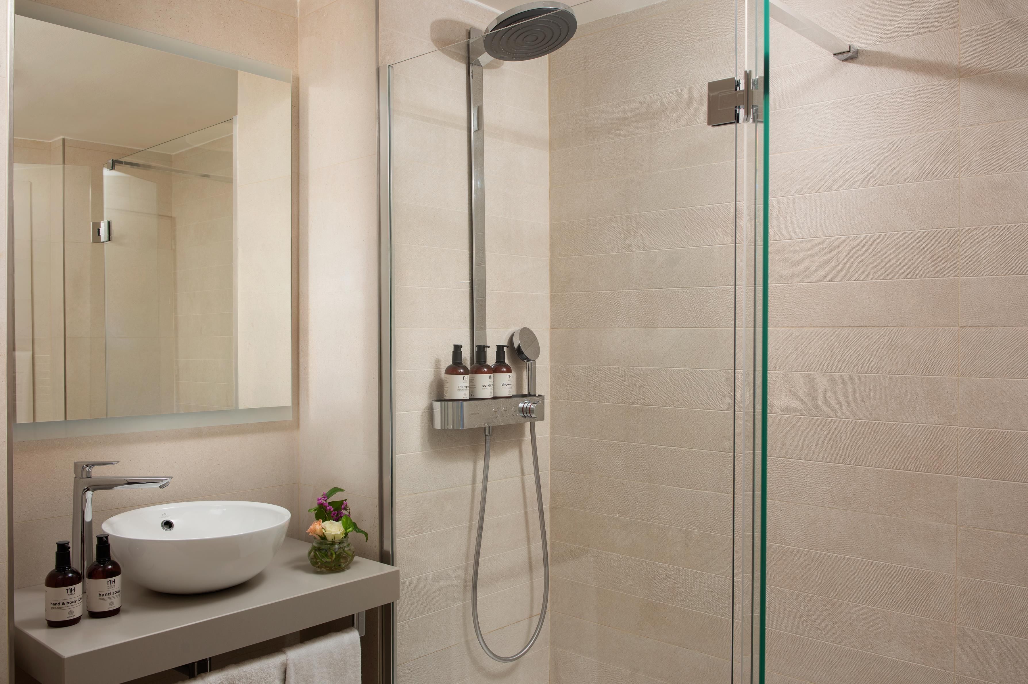 Une salle de bain moderne avec une douche à parois de verre, un lavabo agrémenté d’un vase de fleurs et des articles de toilette disposés sur le comptoir.