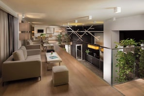 A modern living room with a sofa, ottoman, and coffee table. There is a dining area with chairs and a table. The room has a fireplace and a large window.