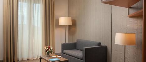 A modern hotel room with a sofa, a small table with a vase of flowers, two floor lamps, and a herringbone-patterned wall.