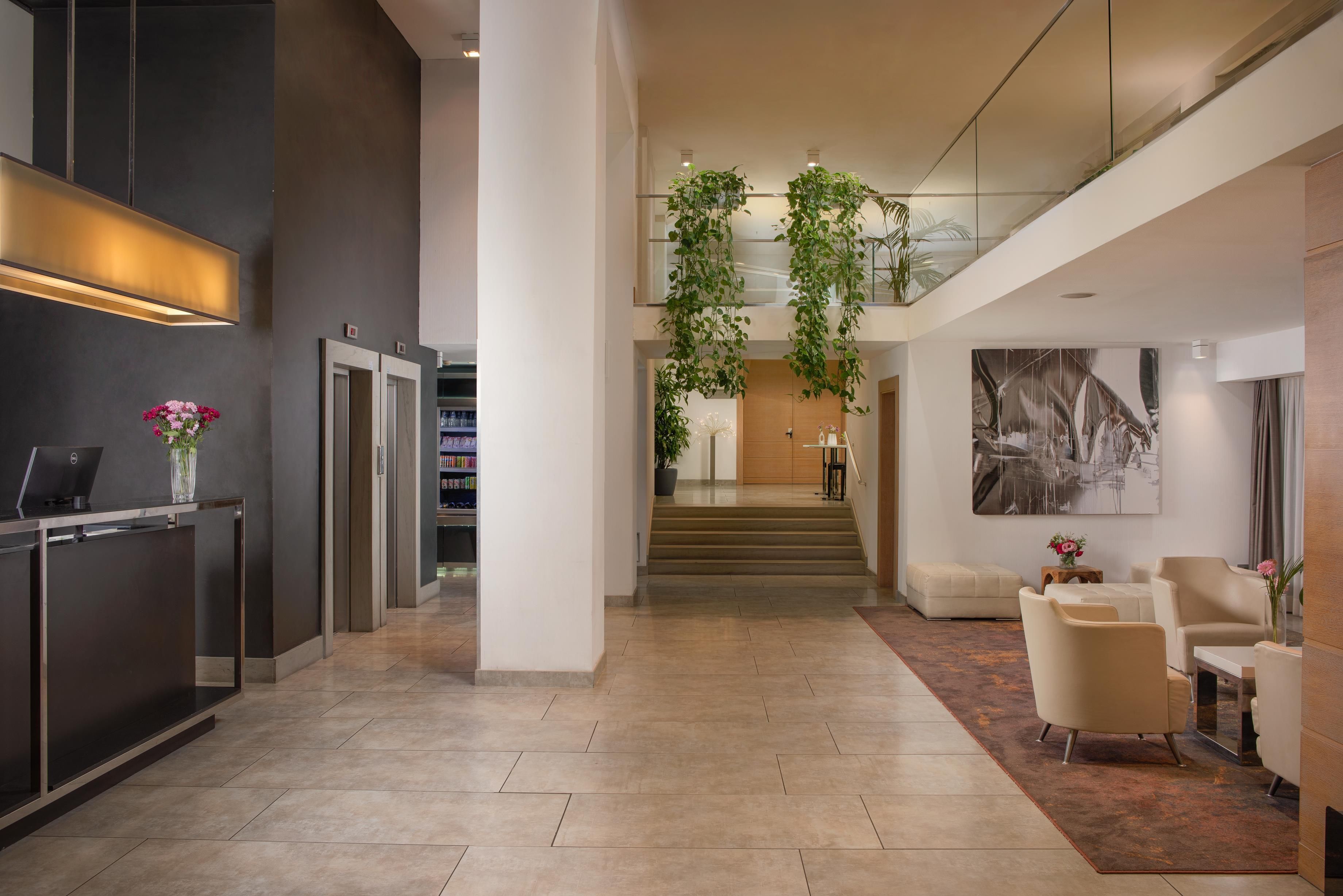 A modern lobby with a reception desk, elevators, a staircase, and a seating area with a large abstract painting.