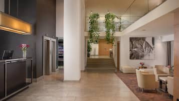 A modern lobby with a reception desk, elevators, a staircase, and a seating area with a large abstract painting.