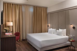 A hotel room with a large bed, a desk with a lamp, a chair, and a small table with a vase.