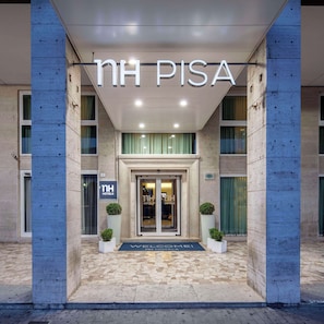 The entrance of NH PISA hotel with a modern design, featuring a stone facade and a welcoming entrance.