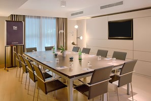 A conference room with a long table, chairs, a projector screen, and a television. - NH Pisa (Pisa)