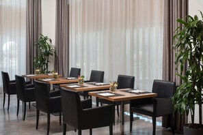 A conference room with long tables, black chairs, and potted plants.