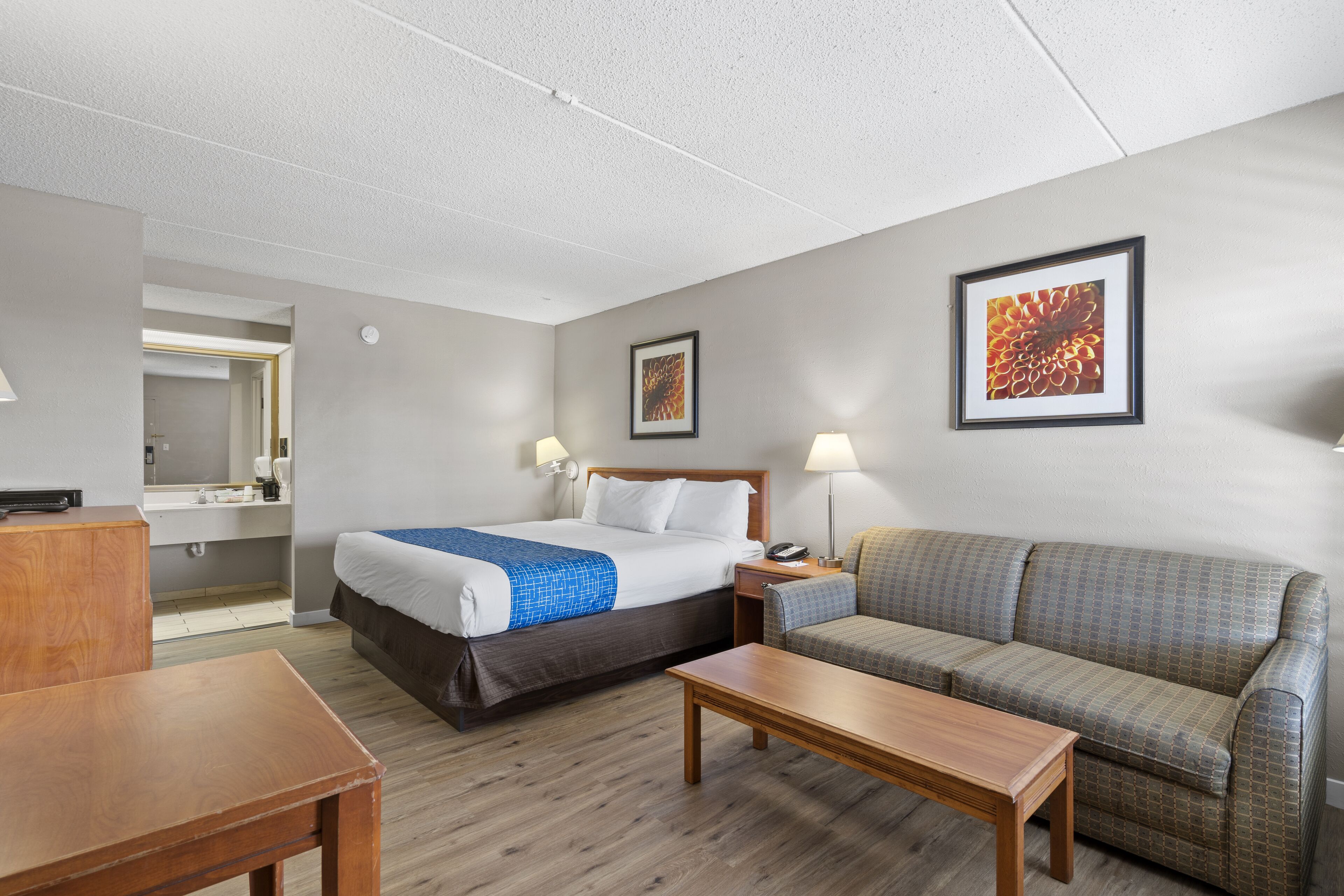 Een hotelkamer met een bed, een bank, een houten tafel, een nachtkastje en een spiegel.