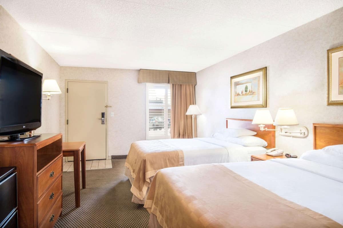A hotel room with two beds, a TV, a desk, and a door.