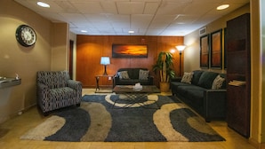 A lobby with a patterned armchair, a sofa, a coffee table, a clock, a lamp, a painting, and a potted plant. - Travelodge by Wyndham Pueblo (Pueblo)