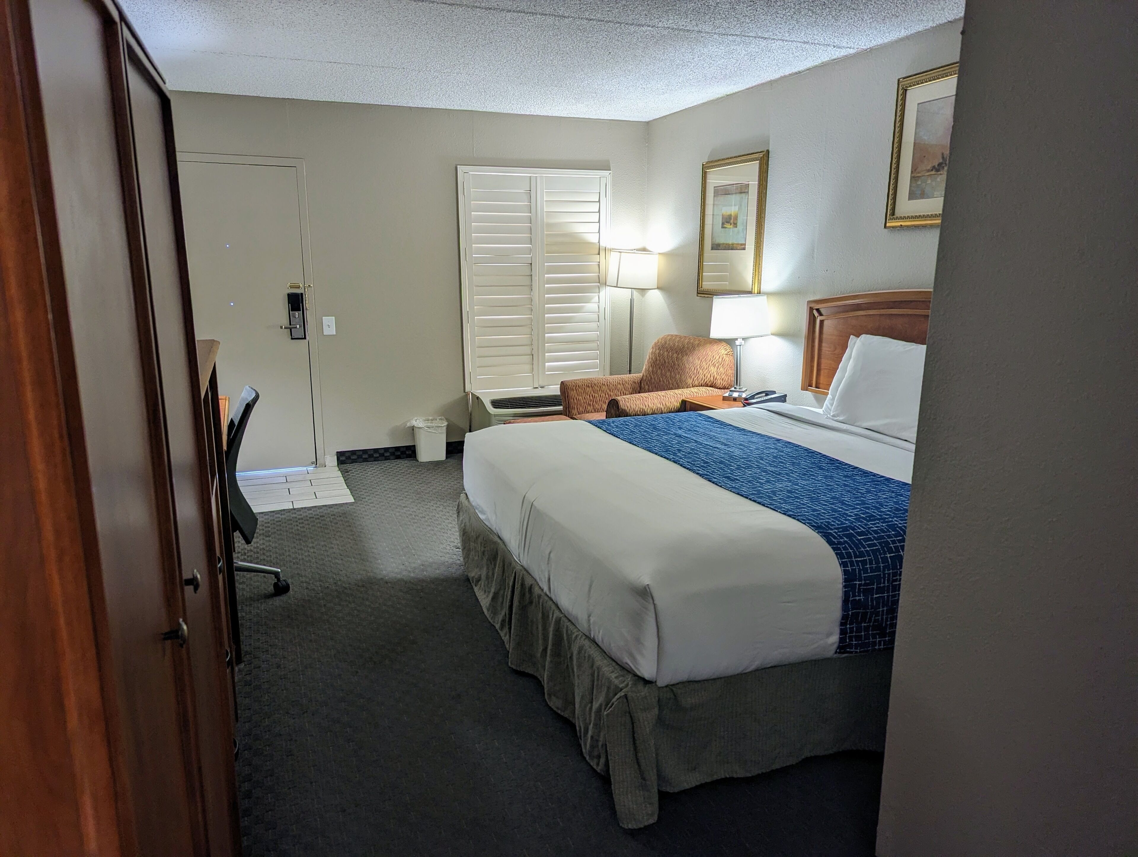 Une chambre d’hôtel avec un lit, une chaise, un bureau, une lampe et un tableau au mur.