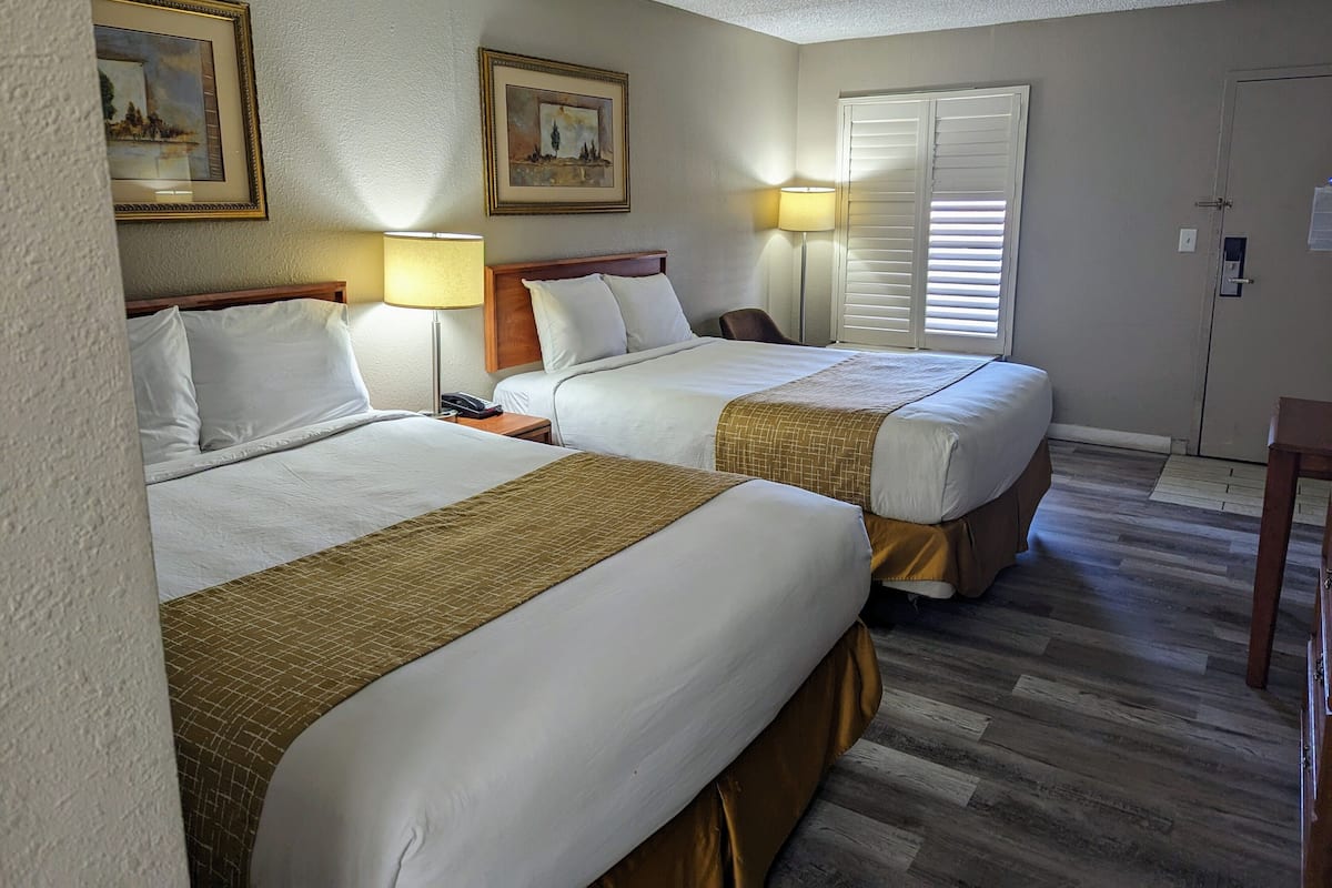 A hotel room with two beds, a nightstand with a lamp, a chair, and a door with a window.