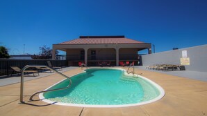 A swimming pool with a metal ladder, surrounded by lounge chairs and a covered seating area. - Travelodge by Wyndham Pueblo (Pueblo)