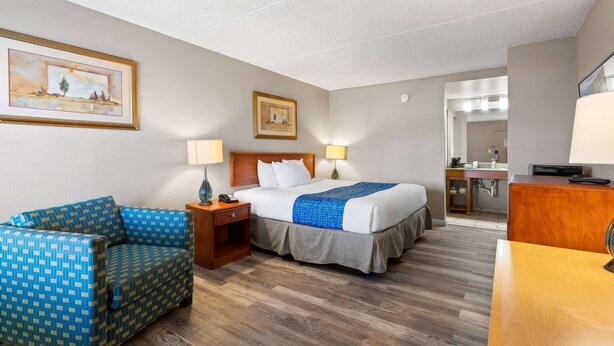 A hotel room with a bed, a sofa, a desk, and a bathroom visible through an open door. - Travelodge by Wyndham Pueblo (Pueblo)