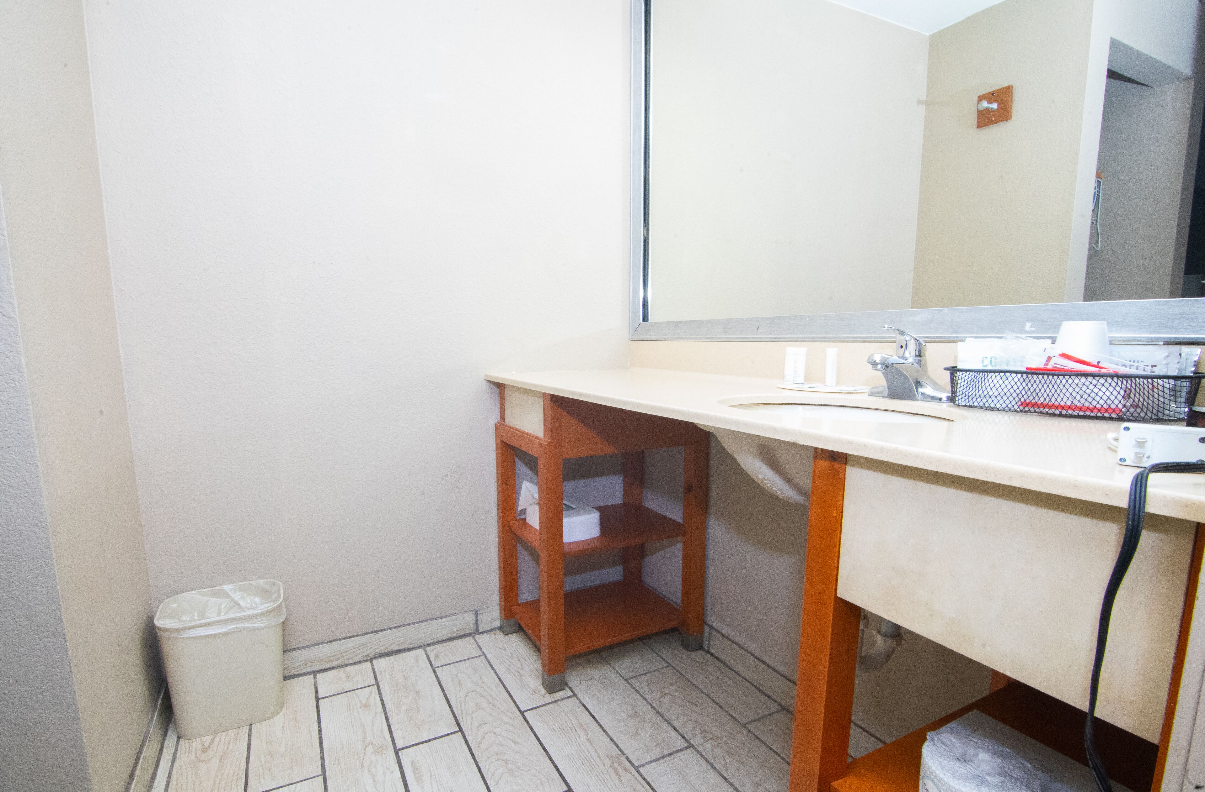 Een kleine badkamer met een houten kruk, een prullenbak en een spiegel.