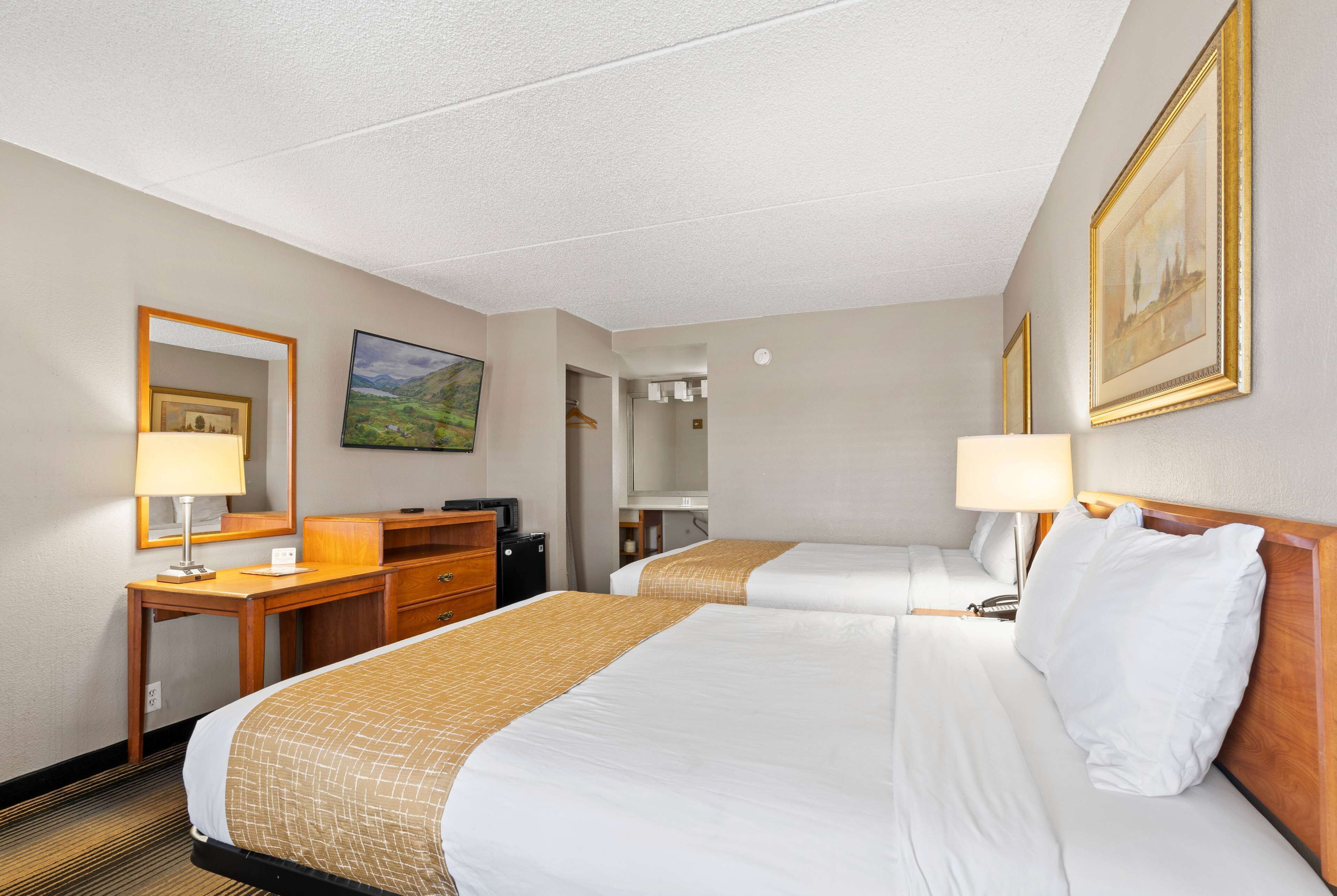 Ein Hotelzimmer mit zwei Betten, einem Schreibtisch, einem Schminktisch und einem Spiegel.