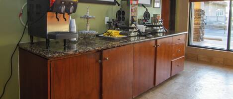 A kitchen with a coffee machine, a fruit dispenser, and a waffle maker.