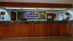 A reception desk with a 'Travelodge by Wyndham' sign, wooden paneling, and two potted plants. - Travelodge by Wyndham Pueblo (Pueblo)