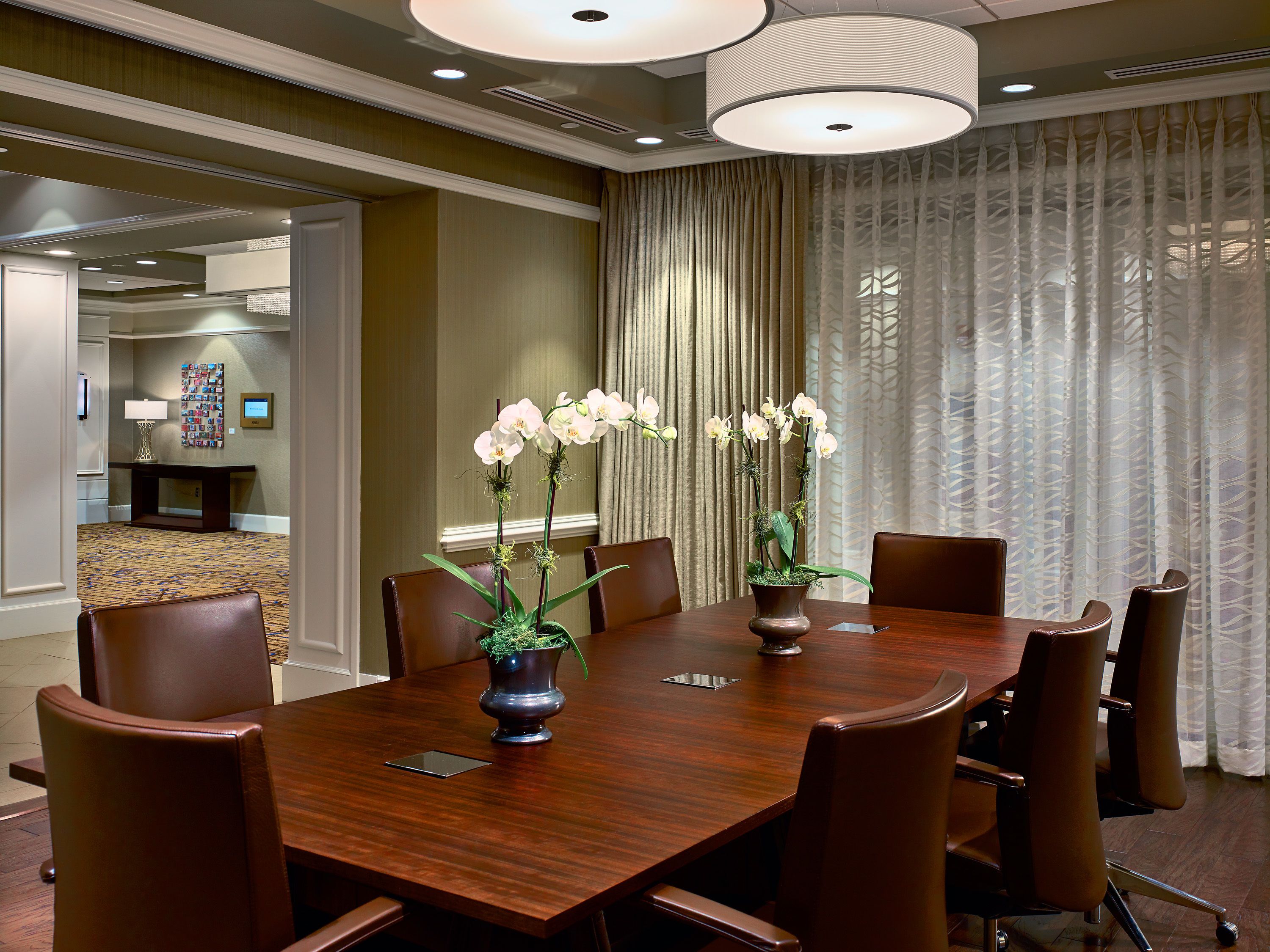 A conference room with a wooden table, brown chairs, and two vases with white orchids.