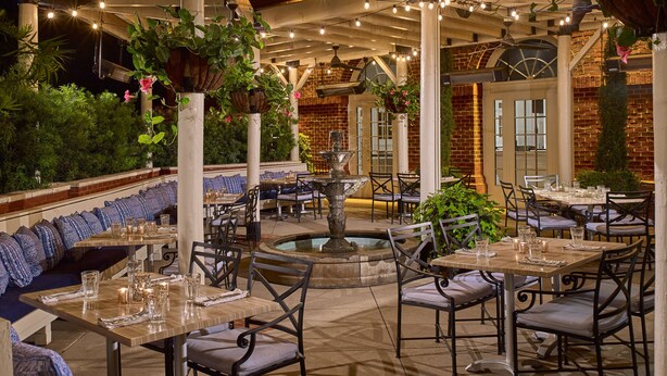 An outdoor dining area with tables and chairs, a fountain, and string lights. - The Hotel At Auburn University (Auburn)