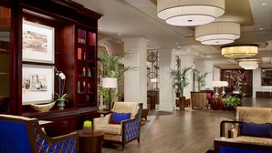 A spacious lobby with a wooden reception desk, framed photographs, and comfortable seating areas. - The Hotel At Auburn University (Auburn)