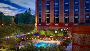 A hotel with a swimming pool, outdoor seating, and a clock tower in the background. - The Hotel At Auburn University (Auburn)