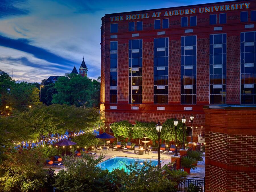 A hotel with a swimming pool, outdoor seating, and a clock tower in the background.