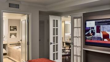 A hotel room with a bed, a TV, a desk, and a bathroom visible through an open door.